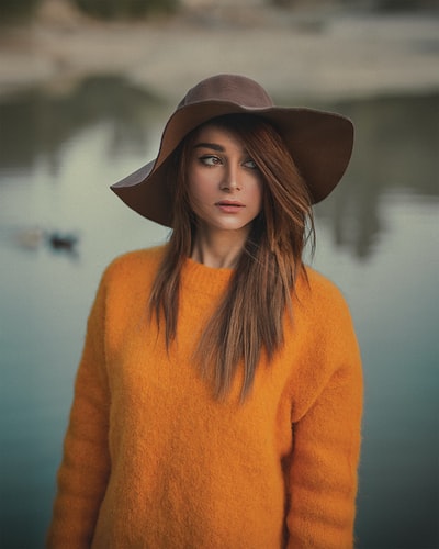 女人穿着橙色的毛衣和棕色帽子站,面对她的右侧
